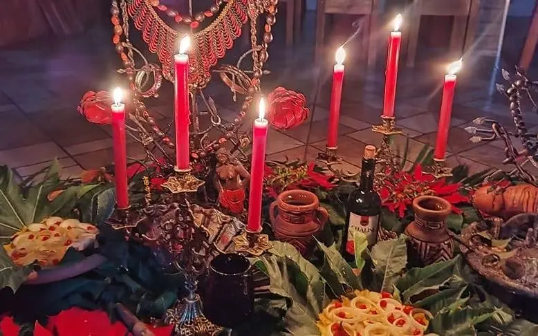Oferenda à noite, com velas vermelhas acesas, flores vermelhas e folhas